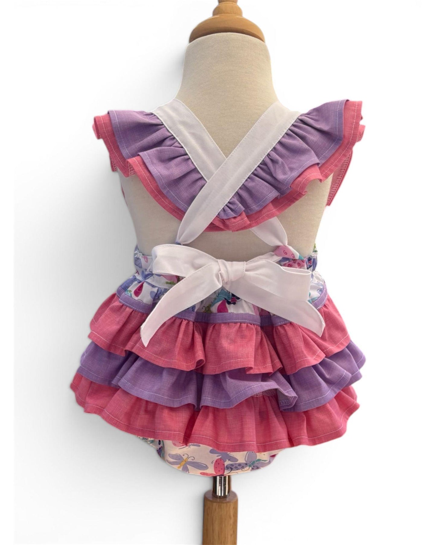 Children's romper with ruffled layers in pink and purple on a mannequin against a white background