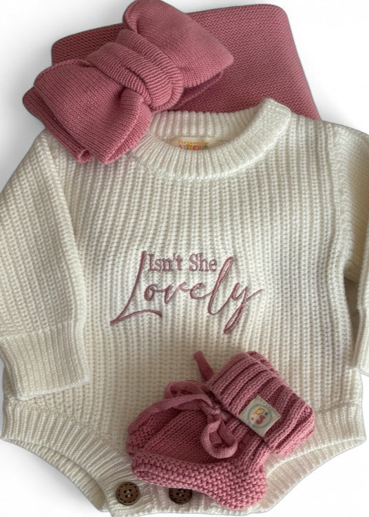Baby sweater with 'Isn't She Lovely' text, pink hat, and booties on a white background