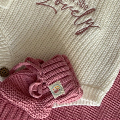 Newborn Baby Isn't She lovely Knit Outfit Flat Lay – Cream rompers with pink and blue embroidered messages, paired with matching baby booties, accessories, and textured knit blankets.