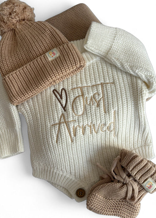 Neutral Knit Newborn Romper Set with “Just Arrived” Embroidery – Includes a cream knit romper, beige pom-pom hat, booties, and matching knit blanket.