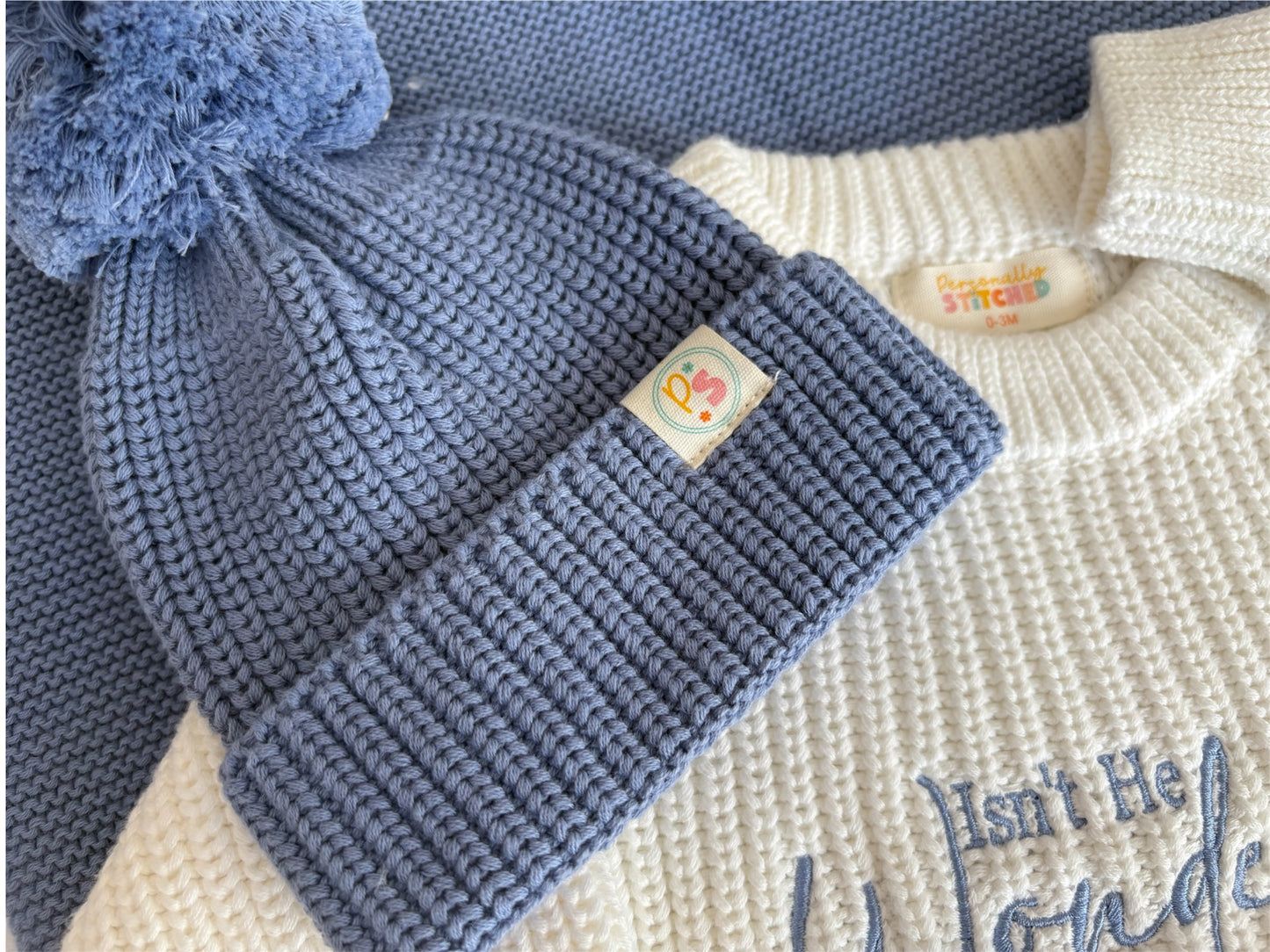 Blue knitted baby hat with a pom-pom on a white background
