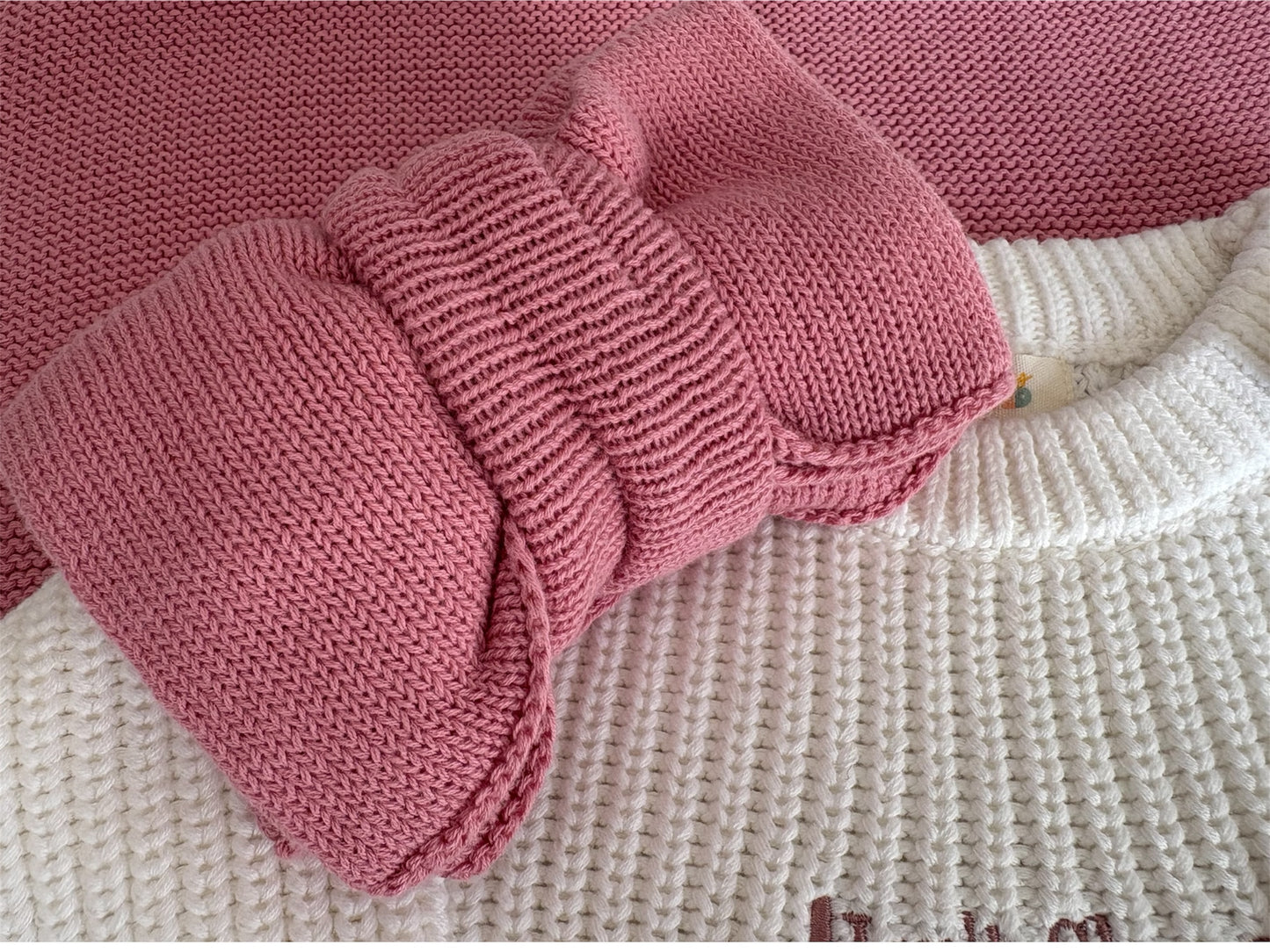 Pink knitted baby booties on a textured surface