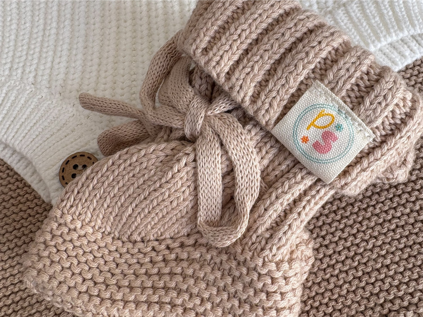 Knitted beige baby bootie with a decorative label on a neutral background