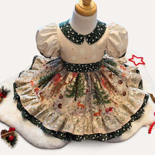 A baby girl's Christmas-themed dress displayed on a mannequin torso. The dress features a cream-colored bodice with white snowflakes, puffy sleeves, and a dark green patterned Peter Pan collar.