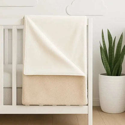 White crib with a beige double sided fleece blanket draped over it, embroidered with custom name.