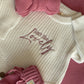 Newborn Baby Isn't She lovely Knit Outfit Flat Lay – Cream rompers with pink and blue embroidered messages, paired with matching baby booties, accessories, and textured knit blankets.