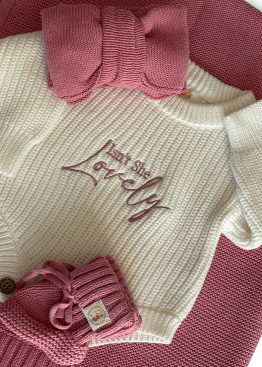 Newborn Baby Isn't She lovely Knit Outfit Flat Lay – Cream rompers with pink and blue embroidered messages, paired with matching baby booties, accessories, and textured knit blankets.