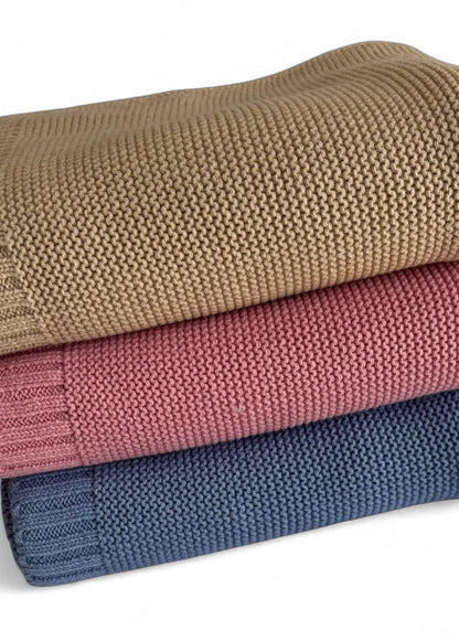 Three stacked knit blankets in beige, pink, and blue on a white background