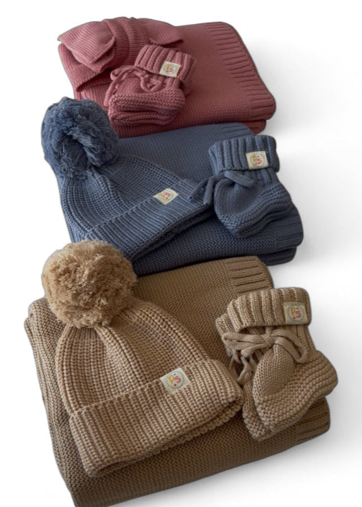 Stack of winter accessories including hats and mittens on a white background