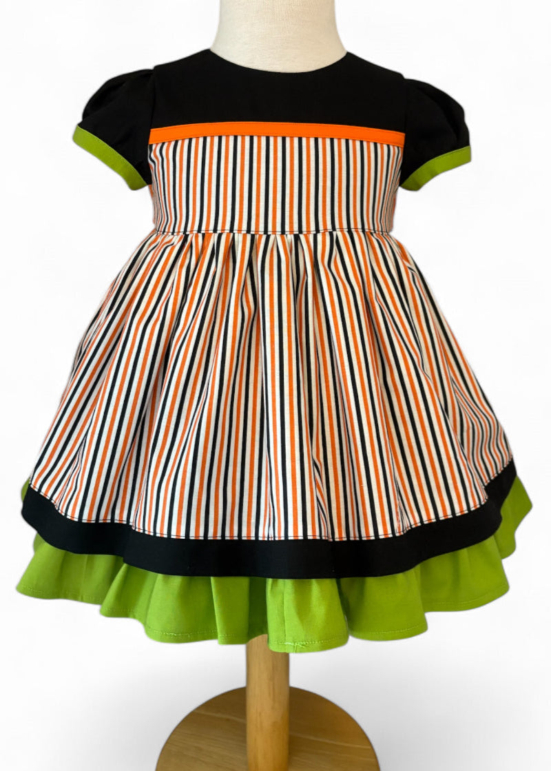 Handmade toddler Halloween dress – black bodice with orange accent, puff sleeves with green trim, and striped orange, black, and white twirl skirt.
