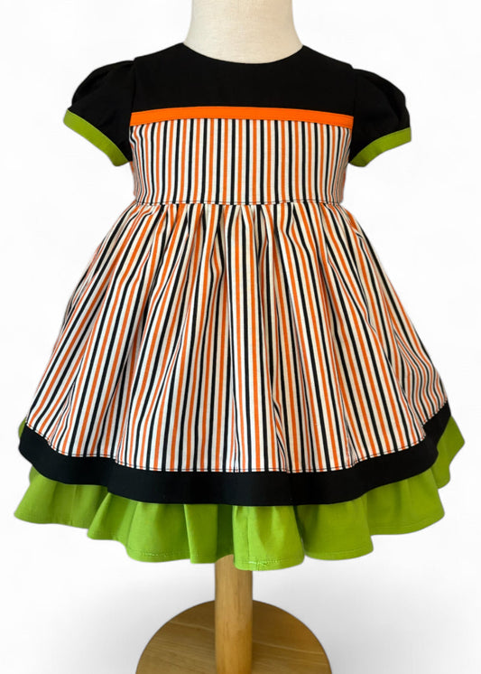 Handmade toddler Halloween dress – black bodice with orange accent, puff sleeves with green trim, and striped orange, black, and white twirl skirt.
