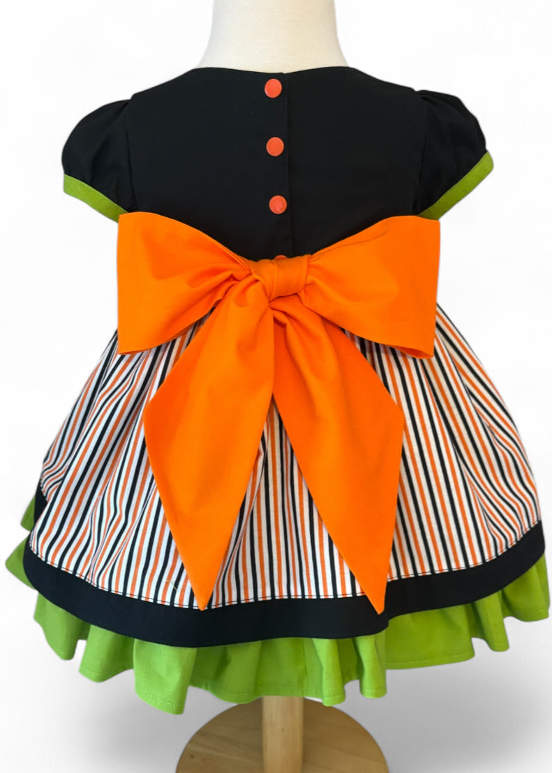 Back view of girls Halloween party dress – features orange buttons, a large bow, and striped skirt with layered green underskirt.