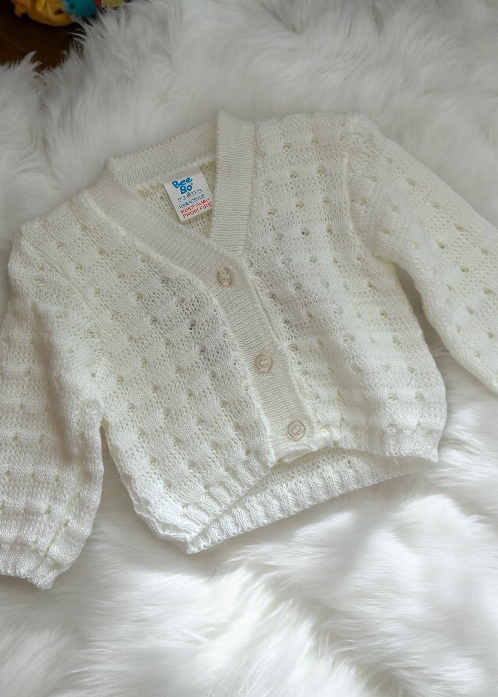 White baby cardigan on a fluffy white surface