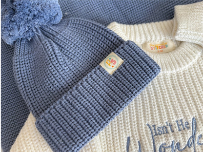 Blue knitted baby hat with a pom-pom on a white background