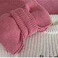 Pink knitted baby booties on a textured surface