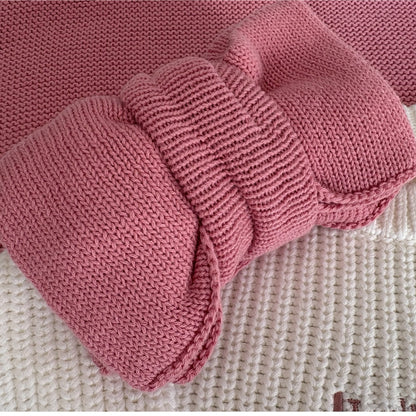 Pink knitted baby booties on a textured surface