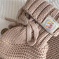 Knitted beige baby bootie with a decorative label on a neutral background
