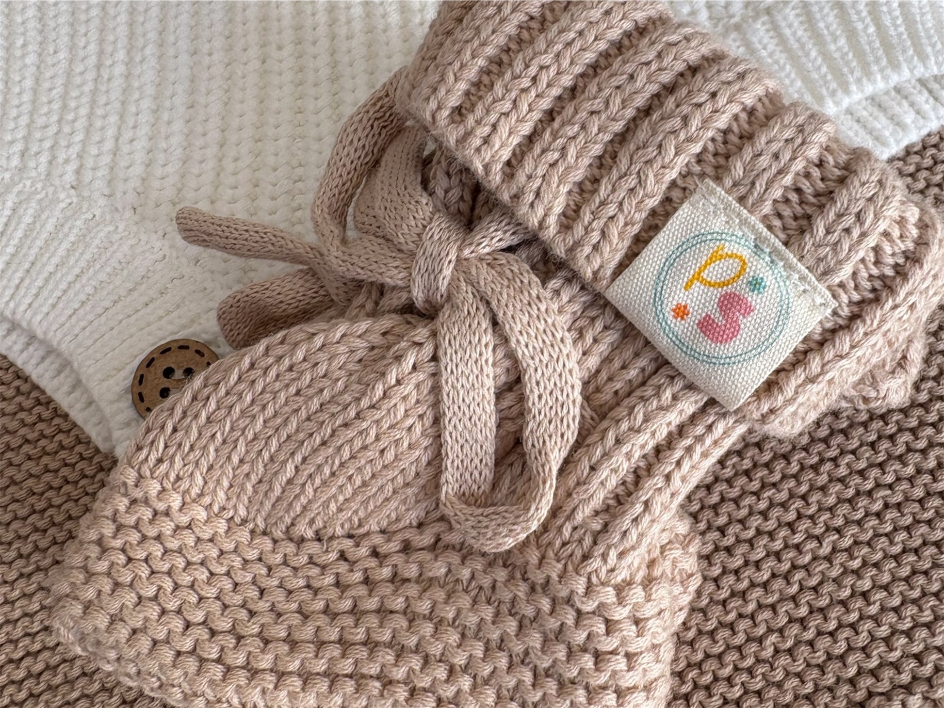 Knitted beige baby bootie with a decorative label on a neutral background