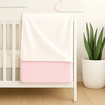 White crib with a pink double sided fleece blanket draped over it, embroidered with custom name.