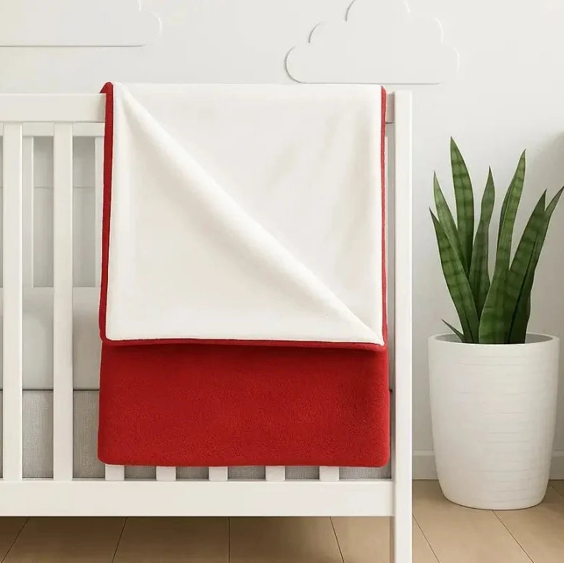 White crib with a red double sided fleece blanket draped over it, embroidered with custom name.