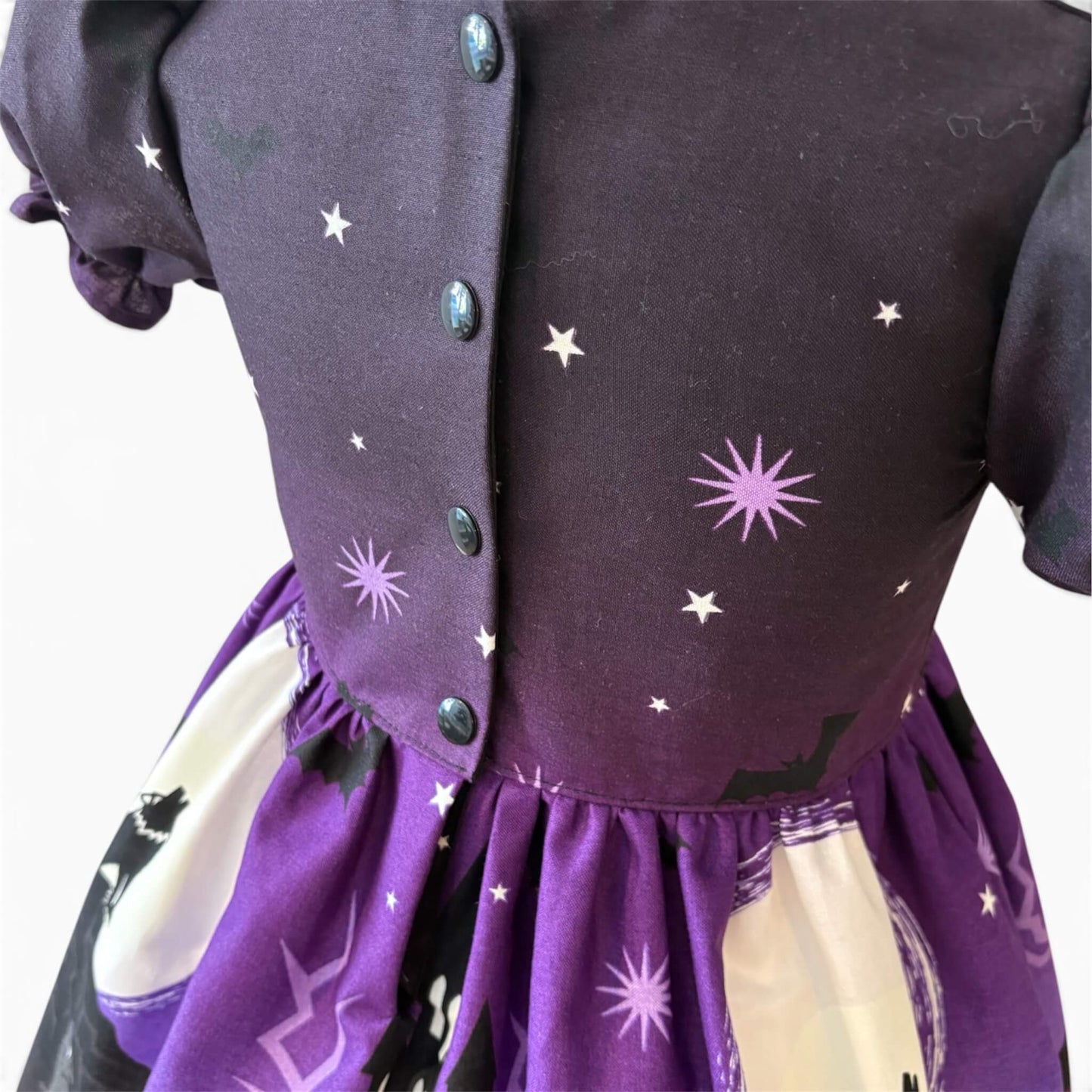 Close-up of the back of a children's dress with a dark purple bodice featuring black popper closure for easy dressing
