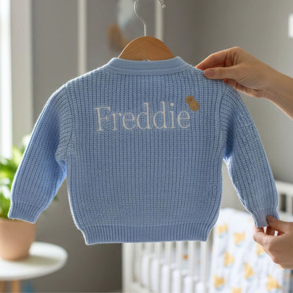 a blue baby cardigan with the baby name embroidered on the back and a little embroidered peanut next to the name 