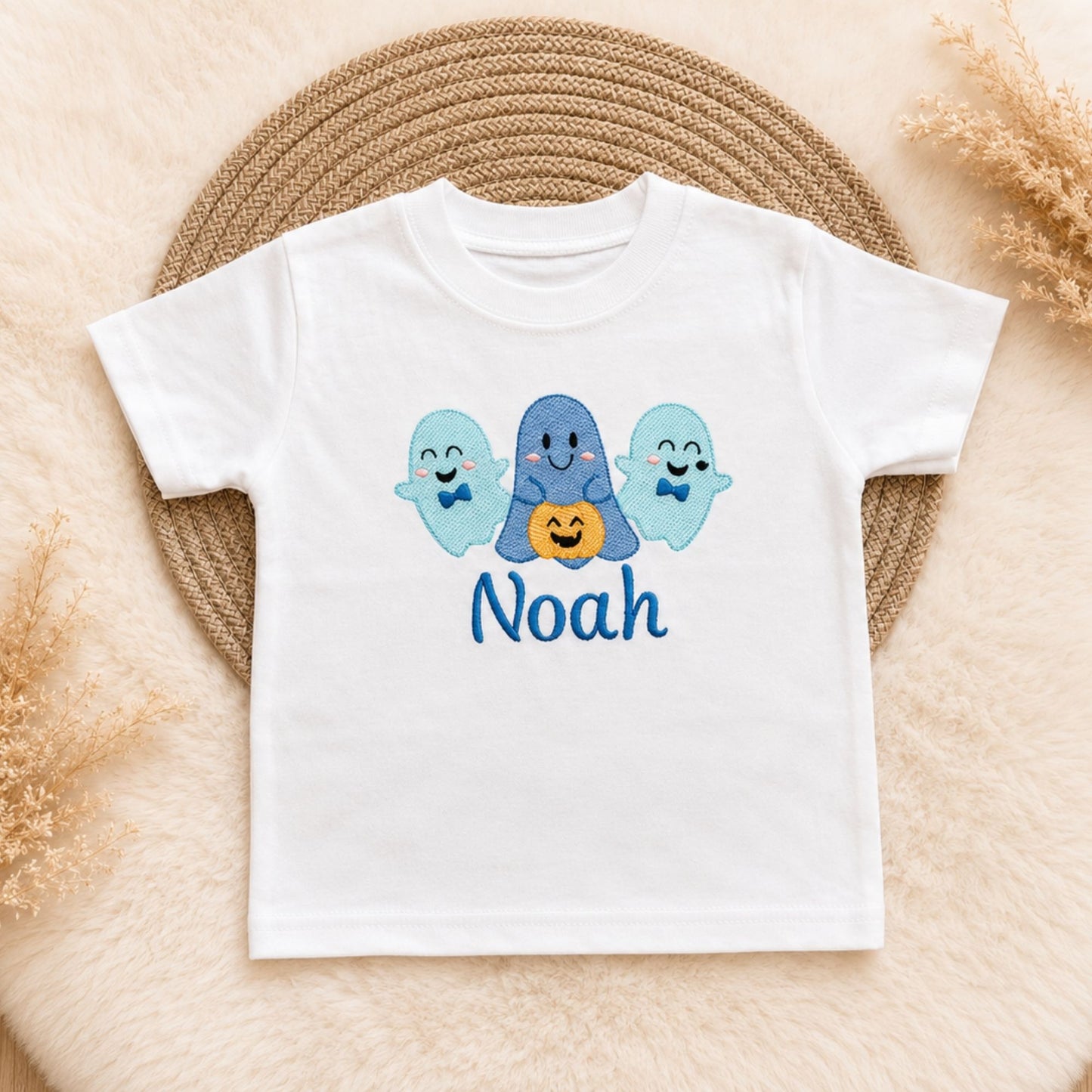 A white short-sleeve kids' t-shirt with a graphic of three blue ghosts and an orange pumpkin, personalised with the name underneath in blue.