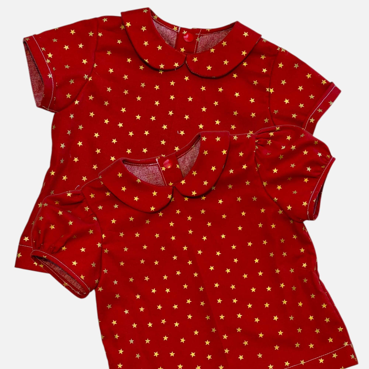 Two red short-sleeve tops with a gold star pattern and Peter Pan collars, displayed on a light gray background.