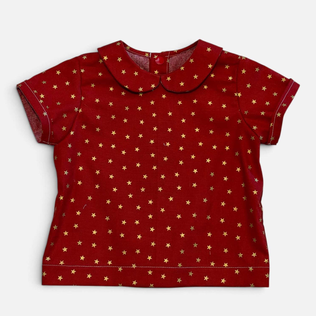 A red short-sleeve baby top with a Peter Pan collar, featuring an all-over gold star pattern, laid flat against a light gray background.