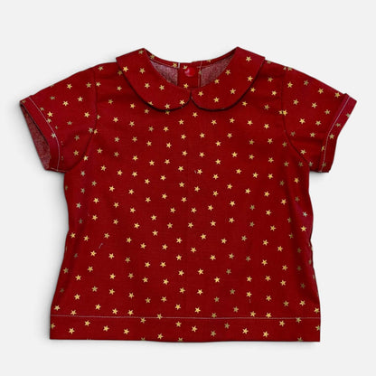 A red short-sleeve baby top with a Peter Pan collar, featuring an all-over gold star pattern, laid flat against a light gray background.