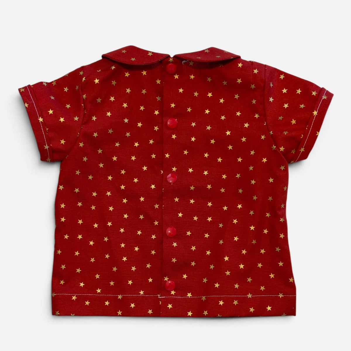 A red short-sleeve button-up shirt with a repeating pattern of small gold stars, laid flat against a light gray background.