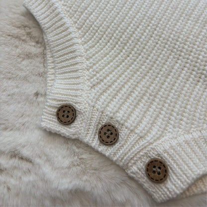 Close-up of a white-coloured knit baby romper with three brown wooden buttons, laid flat on a soft white faux fur surface.