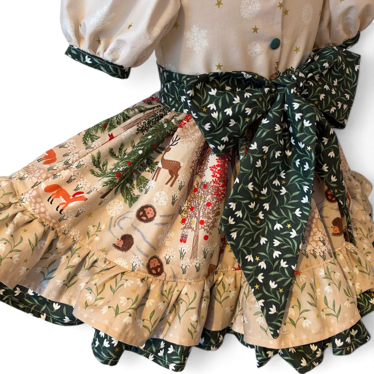 Close-up of the Snowdrop dress’s green snowdrop-print bow above a woodland skirt featuring deer, foxes, hedgehogs and Christmas trees.