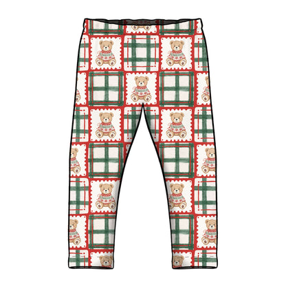 A pair of children's leggings with an all-over Christmas-themed pattern featuring teddy bears in sweaters inside postage stamp designs and green plaid borders, shown against a plain white background.