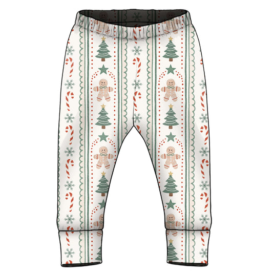 A pair of baby pants with an all-over Christmas pattern featuring gingerbread men, Christmas trees, candy canes, and snowflakes on an off-white background.
