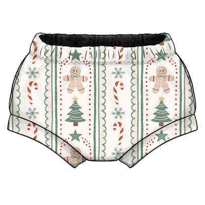 A pair of shorties/bummies with a festive Christmas print, featuring gingerbread men, candy canes, snowflakes, and Christmas trees on a cream background with an elastic waistband.