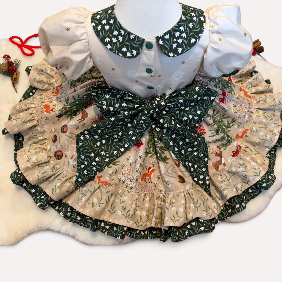Back of the Snowdrop Christmas dress with green popper fastenings, a large green floral bow and a woodland-print skirt spread out to show the ruffled hem.