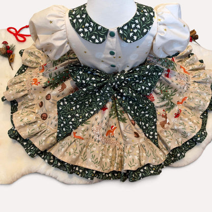 Back of the Snowdrop Christmas dress with green popper fastenings, a large green floral bow and a woodland-print skirt spread out to show the ruffled hem.