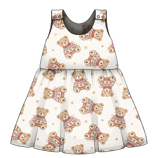 A sleeveless baby dress with a white background and an all-over print of teddy bears wearing red and green knit sweaters, accented with small gold stars.