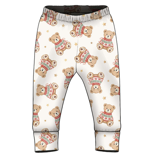 A pair of children's pants with an all-over print of teddy bears wearing red and green sweaters, set against a plain white background.