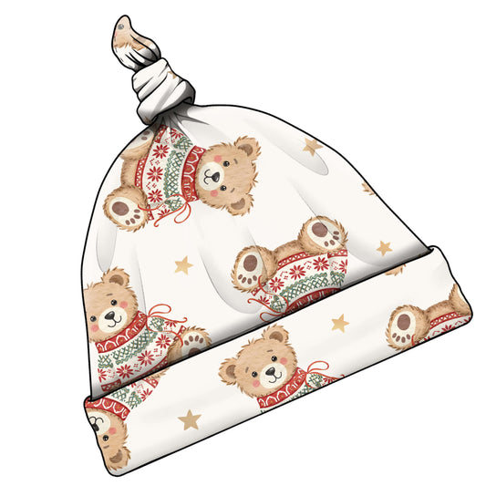 A knotted baby beanie hat featuring a repeating pattern of cute teddy bears wearing festive red and green knit sweaters, with small gold stars on an off-white background.