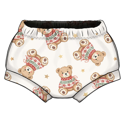 A pair of baby shorts with an all-over print of teddy bears wearing Christmas sweaters and gold stars, on a white background.