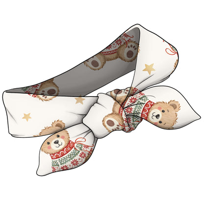 A fabric hair bow featuring a repeating pattern of teddy bears wearing red and green holiday sweaters, accented with small gold stars, shown on a plain white background.