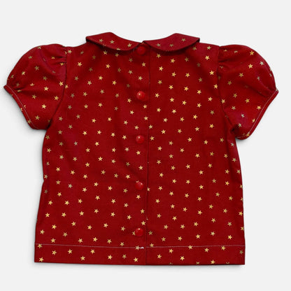 A red short-sleeve baby top with a gold star pattern, featuring a Peter Pan collar and front button closure, laid flat on a light gray background.
