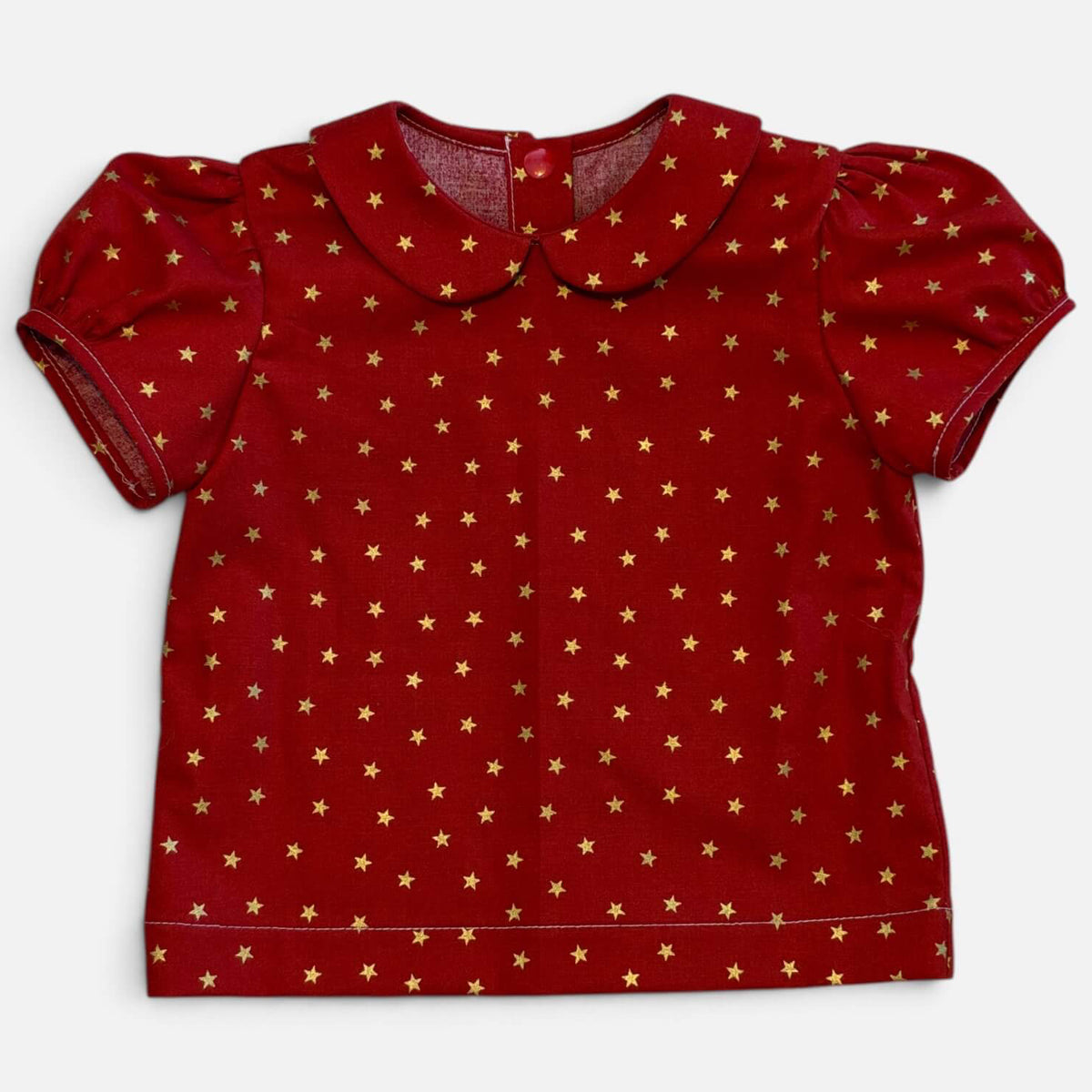 A red short-sleeve baby top with a Peter Pan collar and an all-over gold star pattern, laid flat against a light gray background.