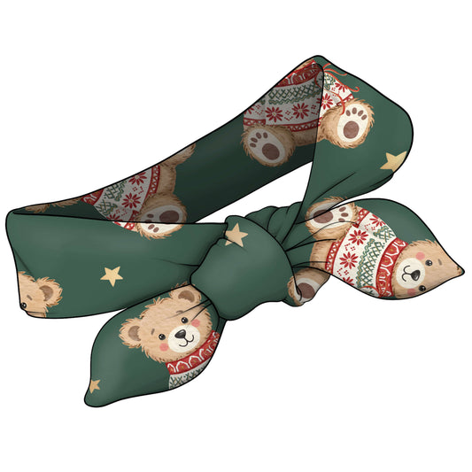 A dark green fabric headband with a repeating pattern of teddy bears wearing red and white knit sweaters and gold stars, shown tied in a bow on a plain white background.