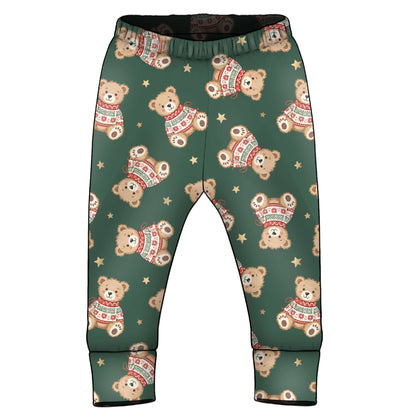 A pair of toddler pants with an all-over print of teddy bears wearing Christmas sweaters and small gold stars on a dark green background.