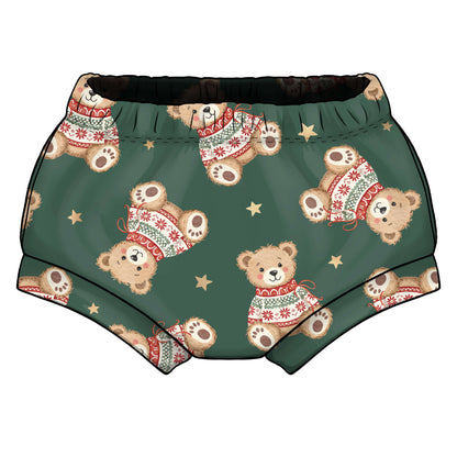 A pair of green children's shorts featuring a repeating pattern of teddy bears wearing red and white holiday sweaters, accented with small gold stars and elasticted waist 