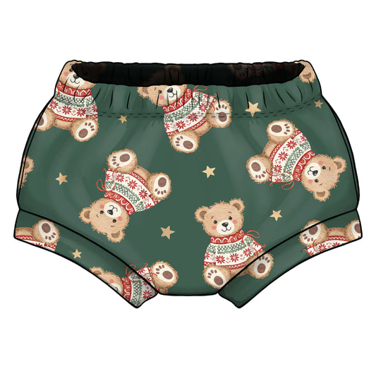 A pair of green children's shorts featuring a repeating pattern of teddy bears wearing red and white holiday sweaters, accented with small gold stars and elasticted waist 