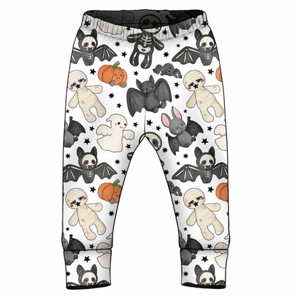 White children's pants with a Halloween-themed print featuring cartoon bats, skeletons, pumpkins, ghosts, and stuffed animals, shown on a plain white background.